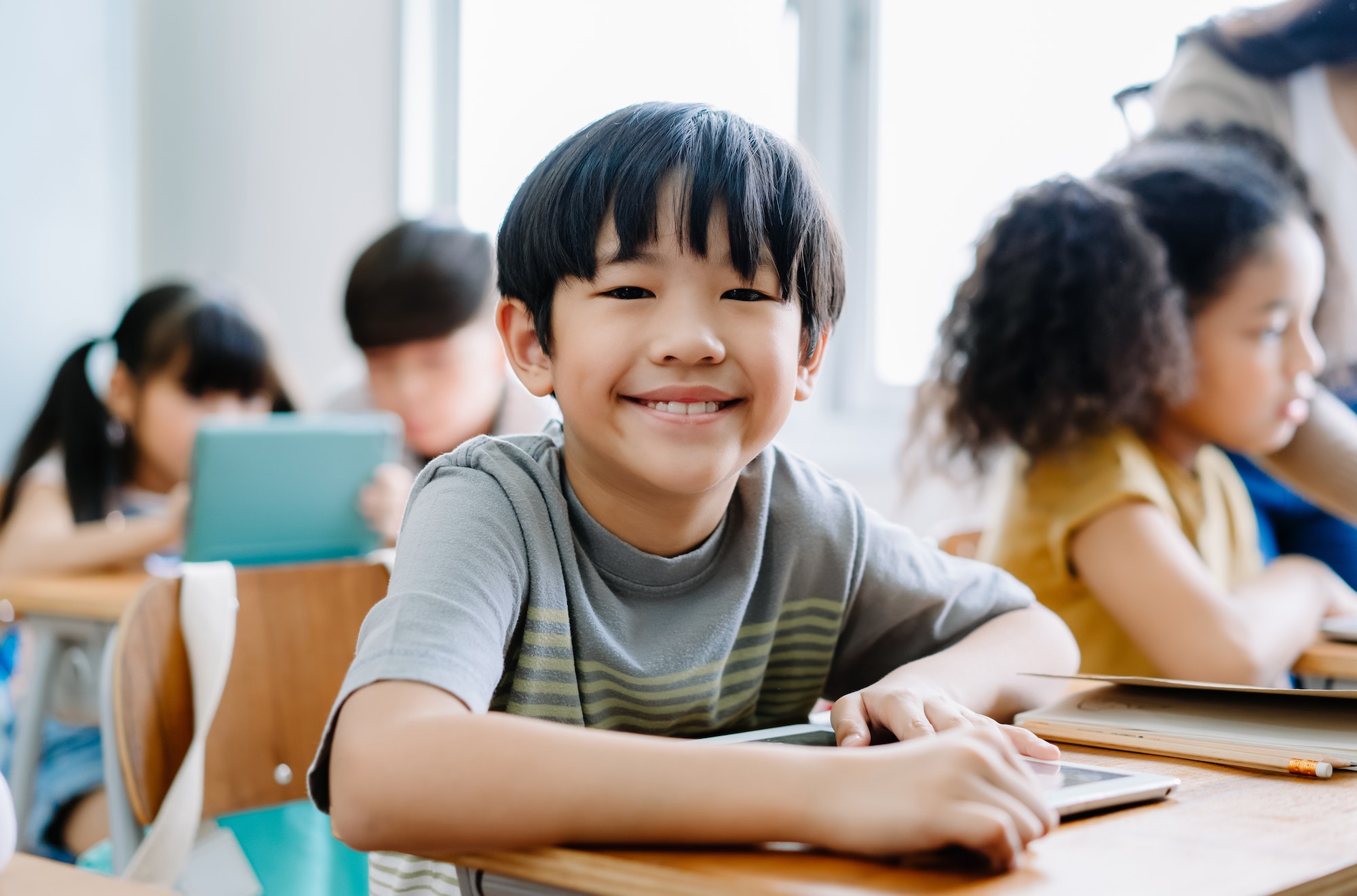 Asian boy smiling looking at camera and using laptop in computer class at the elementary school